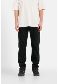 Pantaloni neri a fantasia con un sottile design di logo ripetuto, realizzati in un tessuto morbido, abbinati a una camicia oversized in crema semplice.