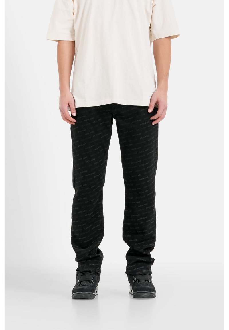 Pantaloni neri a fantasia con un sottile design di logo ripetuto, realizzati in un tessuto morbido, abbinati a una camicia oversized in crema semplice.