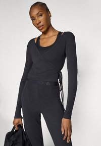 Fekete sportos felső hosszú ujjakkal, testhez simuló szabással és texturált anyagból, hozzá illő, magas derekú nadrággal párosítva.