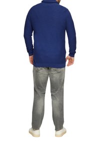 Niebieski polar z długim rękawem i kołnierzykiem, w połączeniu z jasnoszarymi dżinsami i białymi sneakersami, widziany z tyłu. Gładka tekstura, styl casual.