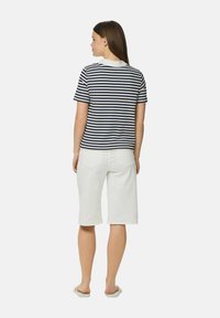 Svītrots t-krekls jūras zilā un baltā krāsā, apvienots ar baltām bermudu biksēm. Gluds kokvilnas audums, standarta piegriezums, īsas piedurknes, minimālas detaļas.