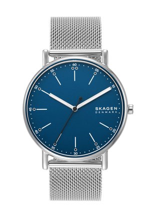 Montre ronde Skagen avec un cadran bleu, des index des heures en argent et un bracelet en maille en acier inoxydable. Design minimaliste, sans marqueurs numériques, finition élégante.
