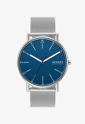 Reloj Skagen redondo con dial azul, marcadores de hora plateados y correa de malla de acero inoxidable. Diseño minimalista, sin marcadores numéricos, acabado elegante.