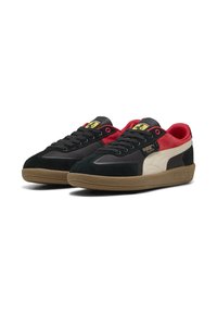 Puma sneakers med en overdel i sort ruskind, røde accenter og en cremet sidepanel. Har gummisål og sorte snørebånd. Guld logo detalje.
