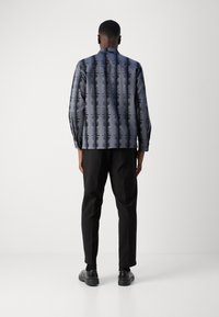 Camisa de manga longa em azul com um padrão vertical preto, combinada com calças e sapatos pretos, apresentando um corte descontraído e uma textura suave.