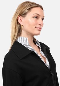 Mustmust lahtise kraega must zip-up jakk, mille alla on kantud valge ja tumesinise triibuga särk. Jakk on sileda tekstuuriga ja korraliku lõikega.