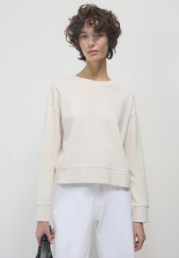 Felpa cropped beige chiaro realizzata in tessuto morbido, con maniche lunghe e scollo rotondo, abbinata a jeans bianchi a vita alta.