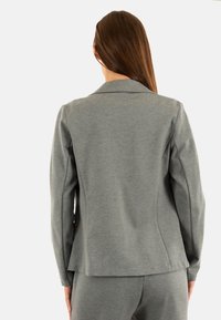 Blazer gris ajustado hecho de tela suave. Presenta un cuello con muesca y hombros estructurados, con una silueta entallada y una textura suave.