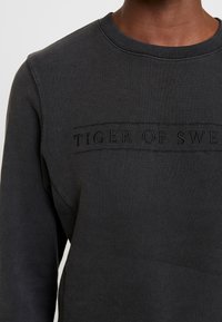 Felpa nera con scollo rotondo e logo "TIGER OF SWEDEN" in rilievo sul petto. Realizzata in tessuto morbido, con un design a vestibilità regolare.