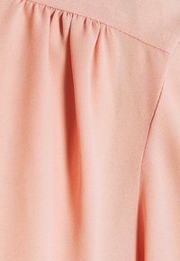 Tissu rose doux avec un détail de couture froncée, montrant la texture et les coutures en gros plan.