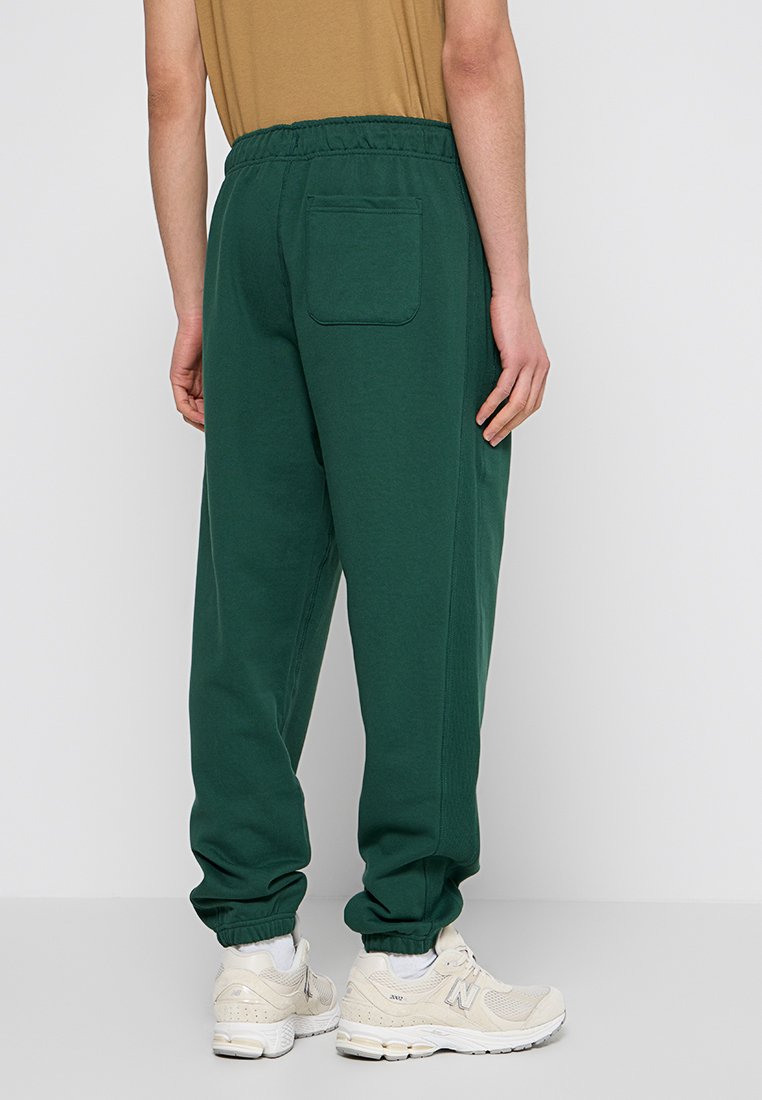 Pantaloni della tuta verdi in tessuto morbido con cintura elastica, gambe affusolate e tasca posteriore. Abbinati a sneaker chiare.