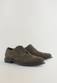 Brązowe zamszowe buty typu brogue z zasuwanymi sznurówkami, z perforowanymi detalami, gładką czarną podeszwą oraz klasycznym kształtem.