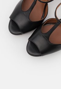 Sandales en cuir noires à bout ouvert avec bride en T et semelles intérieures rembourrées marron, vues de dessus sur fond blanc.