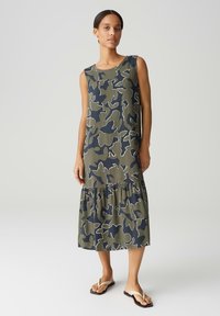 Sleeveless camouflage-print dress in olive green and navy, featuring a tiered ruffle hem and smooth fabric texture.