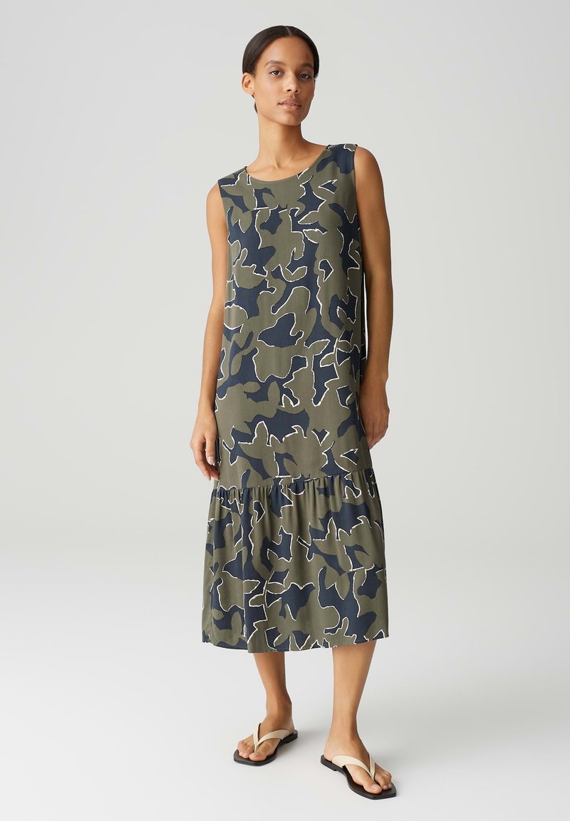 Sleeveless camouflage-print dress in olive green and navy, featuring a tiered ruffle hem and smooth fabric texture.