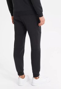 Černé sportovní kalhoty slim fit s texturovanou tkaninou, zúženými nohavicemi a bočními kapsami. Kombinované s bílými sportovními botami.