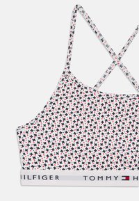 Bralette blanca con un patrón floral en azul marino, rojo y negro. Tiras delgadas que se cruzan en la parte posterior. Presenta una banda sólida con el logo "TOMMY HILFIGER".