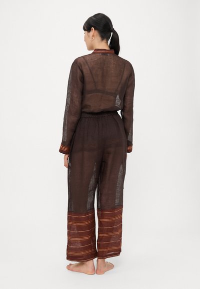 Pruun linakiust kombinesoon läbipaistva kangaga, kummipaelaga vöökohaga, pikkade varrukatega ja värviliste triipudega ääres. Alasti jalaga modell vaadatuna tagantpoolt.