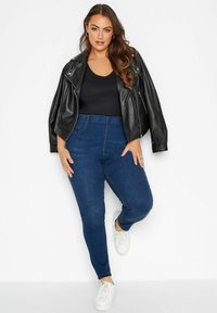 Musta tekonahkainen lyhyt takki, tiukka musta paita, siniset korkeavyötäröiset skinny-farkut ja valkoiset nauhakengät.