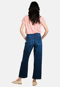 Jeans ampi di colore blu scuro con vita alta, abbinati a una maglietta a maniche corte di colore rosa chiaro. Design semplice, senza motivi visibili o elementi in metallo.