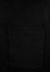 Black knitted sweater fabric with a soft texture. Features a front pocket with ribbed edging, consistent color and pattern throughout.