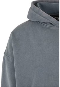 Pullover hoodie i blødt grå stof med en snoretrækshætte, drop shoulder og en glat tekstur. Minimal syning detaljer synlige.