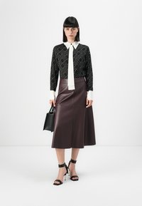Black patterned blouse with white collar and tie, paired with a burgundy leather midi skirt. Black handbag and strapped high heel sandals.