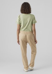 T-shirt en coton vert clair avec manches en dentelle festonnée, associé à un pantalon beige à taille élastique et des baskets de couleur claire. Design simple et décontracté.