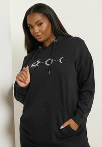 Felpa nera con cappuccio e tasca frontale, decorata con grafiche celestiali bianche: sole, cerchio e luna crescente. Tessuto morbido e design dal taglio rilassato.