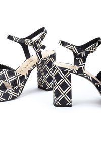 Sandalias de tacón con patrón en blanco y negro, con un acabado texturizado, que presentan tacones gruesos y correas ajustables en el tobillo.