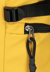 Gelbes Gewebe mit texturiertem Finish verfügt über einen schwarzen Reißverschluss und Zugbänder, sowie einen schwarzen Kunststoffschnalle und Details mit Riemen.