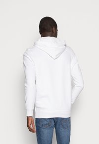 Vit hoodie med avslappnad passform, med ribbade ärmslut och nederkant, tillverkad av mjukt tyg, utan synliga mönster eller grafik.