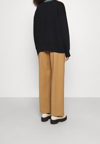 Sudadera negra de gran tamaño con hombros caídos, combinada con pantalones anchos color beige y zapatos gruesos color crema. Textura suave, corte relajado.