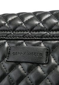 Černá prošívaná kožená kabelka s texturovaným povrchem a výraznou logovou etiketou. Obsahuje vzor ve tvaru diamantu a detaily prošívání.