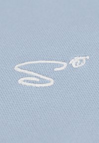 Lichtblauwe stof met een gestructureerde weving en een opvallend wit geborduurd "S"-ontwerp. Zachte textuur met een gladde afwerking.