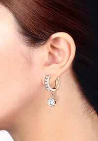 Guldtonad hoopörhänge med små klara rhinestones och en hängande klar ädelsten. Har en polerad yta och säker spänndesign.