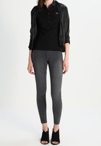 Svart pikétröja med tre knappar, i kombination med en svart bomberjacka, mörkgrå skinny jeans och svarta öppna ankelboots.