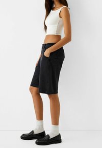 Musta farkkushortsit sivutaskuilla, polvipituinen, yhdistetty valkoiseen lyhyeen puseroon ja mustiin loafereihin, valkoisten ribbineuloksisten sukkien kanssa.