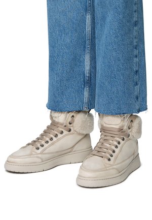 Baskets montantes en cuir beige avec des accents en fourrure, lacets plats et coutures contrastantes, associées à un pantalon en denim bleu coupé.
