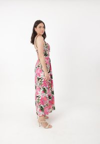 Blomstrete maxi-kjole med et mønster i pink, grøn og hvid, tynde sorte stropper og en flydende silhuet, båret med strappy beige hæle.