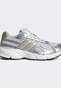 Baskets de sport blanches et argentées avec dessus en mesh, bandes dorées et argentées sur le côté, lacets blancs et semelle blanche rembourrée.