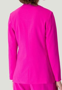 Blazer fuchsia à manches longues et coupe ajustée, avec une texture lisse et des lignes épurées, sans fermetures visibles.