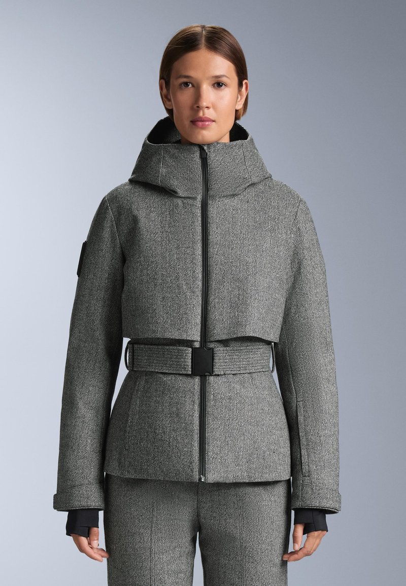 Sivý kabát v rybárskom vzore s vysokým golierom, zipsom vpredu, širokými manžetami a priliehavým opaskom v oblasti pása. Materiál sa zdá byť štruktúrovaný a textúrovaný.