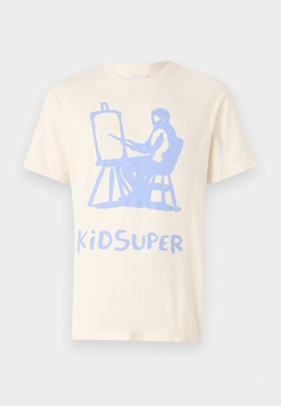 Cremfarbendes Baumwoll-T-Shirt mit einem blauen Grafikmotiv eines sitzenden Figures, die an einer Malerleinwand malt. Darunter befindet sich der Text "KiDSUPER" in derselben Farbe.