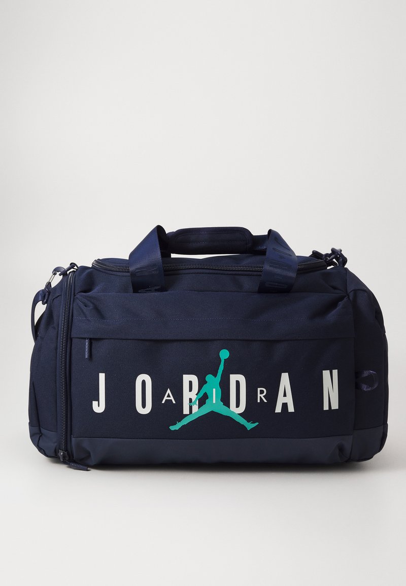 Bolsa de deporte navy con dos asas, tapa con cremallera y llamativo texto en blanco "JORDAN". Presenta el icónico logo del jumpman en aqua. Tejido texturizado.