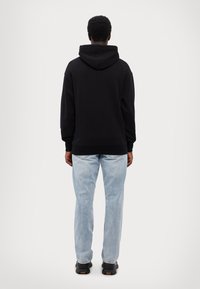 Schwarzer Hoodie mit großer Kapuze, lockerer Passform, gerippten Bündchen und Saum; kombiniert mit hellblauen Jeans und schwarzen Sneakers. Minimalistisches Design.
