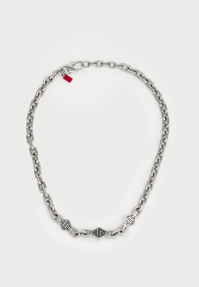 Sølvmetalkæde med flade, sammenkoblede led og diamantformede accenter med sort "HUGO" skrifttype. Inkluderer lås og rød tag.