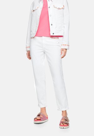 Person wearing white jeans and jacket with colorful trim, pink shirt, and pink glittery sandals with chunky buckles.