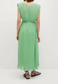 Vestido maxi plisado verde con escote en V, cintura ajustada y tejido fluido. Cuenta con una textura suave y un dobladillo que roza los tobillos.