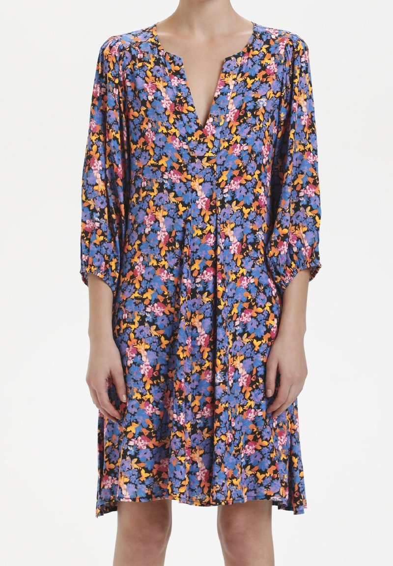 Robe florale avec un fond bleu vif orné de fleurs roses, jaunes et oranges. Décolleté en V, manches trois-quarts, longueur genou.